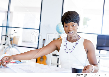 Young woman sitting at a desk in an office and working on blueprint Young woman sitting at a desk in an office and working on blueprint 33867993