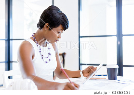 Young woman sitting at a desk in an office and working on blueprint Young woman sitting at a desk in an office and working on blueprint 33868155