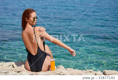 Girl in bikini applying sun lotion at seaside Girl in bikini applying sun lotion at seaside 33877192