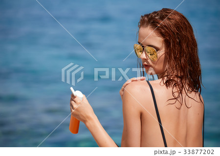 Girl in bikini applying sun lotion at seaside Girl in bikini applying sun lotion at seaside 33877202