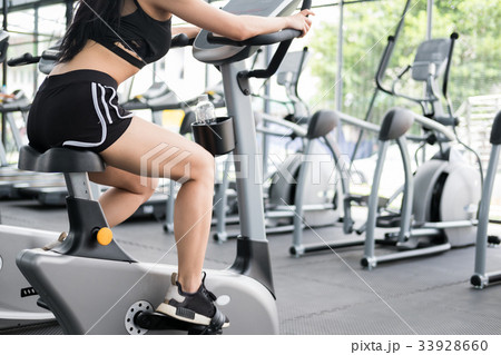 young woman execute exercise in fitness center. female athlete riding stationary bicycle in gym. sporty girl working out in health club. young woman execute exercise in fitness center. female athlete riding stationary bicycle in gym. sporty girl working out in health club. 33928660