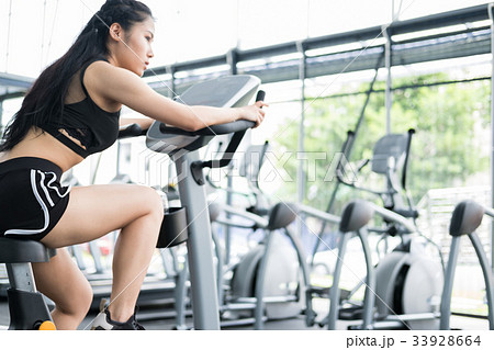 young woman execute exercise in fitness center. female athlete riding stationary bicycle in gym. sporty girl working out in health club. young woman execute exercise in fitness center. female athlete riding stationary bicycle in gym. sporty girl working out in health club. 33928664