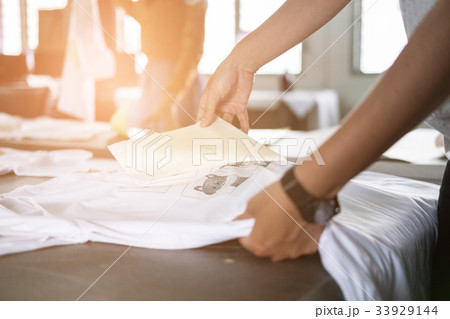 Young woman pull out paper from waterproof film on fabric at shop. worker working on manual screen printing on t-shirt. 33929144
