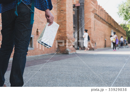 young asian man wearing blue shirt and jeans with map and backpack standing near old brick wall young asian man wearing blue shirt and jeans with map and backpack standing near old brick wall 33929838