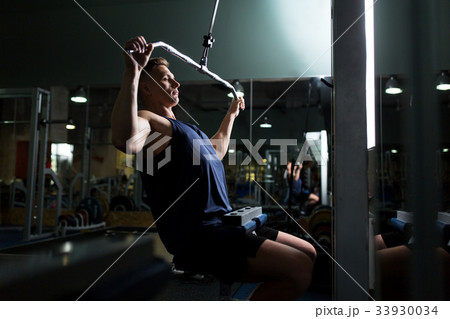 man flexing muscles on cable machine in gym man flexing muscles on cable machine in gym 33930034