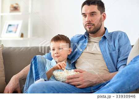 father and son with popcorn watching tv at home father and son with popcorn watching tv at home 33930946