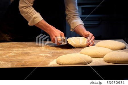 baker portioning dough with bench cutter at bakery 33930981