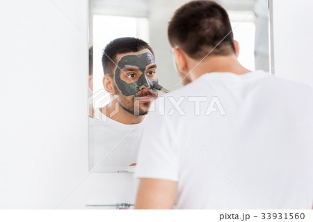young man applying clay mask to face at bathroom 33931560