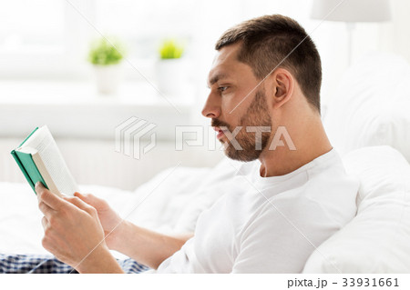 man reading book in bed at home man reading book in bed at home 33931661