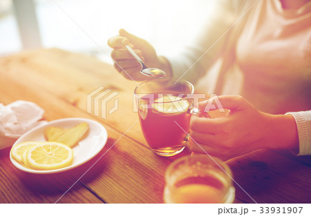 close up of woman adding honey to tea with lemon 33931907