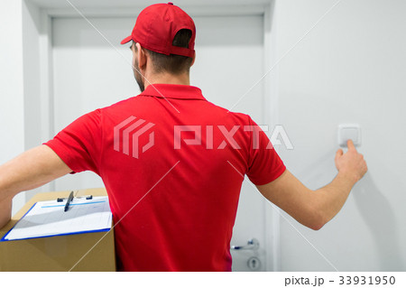 delivery man with parcel box ringing door bell 33931950