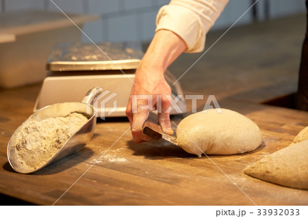 baker portioning dough with bench cutter at bakery baker portioning dough with bench cutter at bakery 33932033