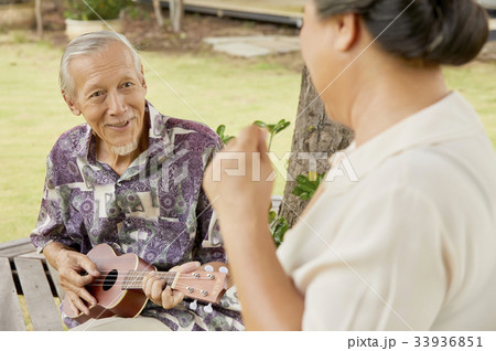 An elderly man is playing guitar and looking at his wife 33936851