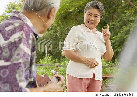 An elderly woman is smiling at her husband and dancing outdoors 33936863