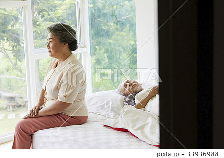 A senior woman is sitting and a senior man is lying on the bed A senior woman is sitting and a senior man is lying on the bed 33936988