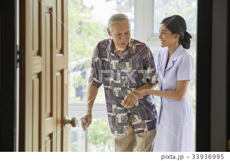 A nurse is helping a senior man to stand beside the door 33936995