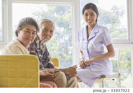 A senior couple and a nurse are sitting and smiling 33937022