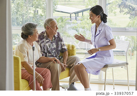 A nurse is sitting and talking to two old patients 33937057