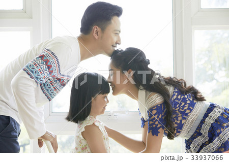 A wife is kissing her daughter 's forehead while the husband is doing the same thing with her. A wife is kissing her daughter 's forehead while the husband is doing the same thing with her. 33937066