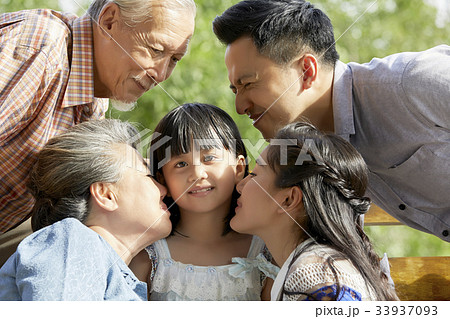 a grandmother and a wife are kissing a little girl, the grandfather and the husband are looking at her. 33937093