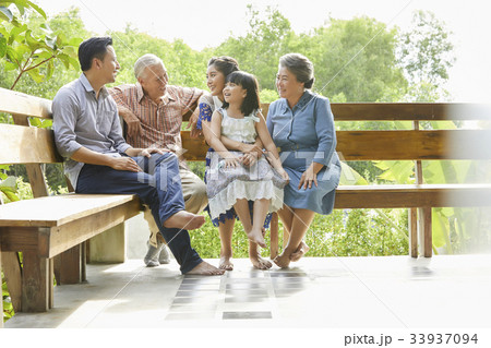 An extended family is sitting, relaxing and having fun on a bench. 33937094