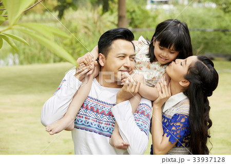 The father is carrying his daughter while the mother is kissing her. 33937128