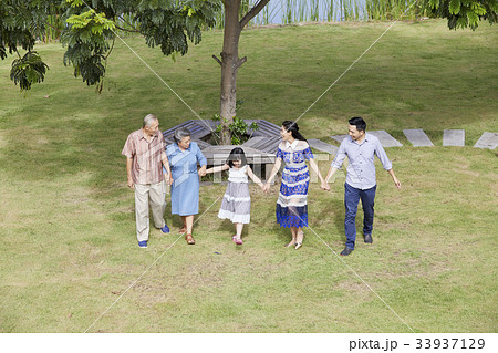an extended family is holding hands and walking on grass. 33937129