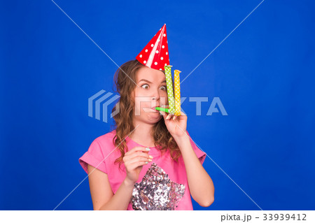 Funny young woman in a birthday cap blowing a 33939412