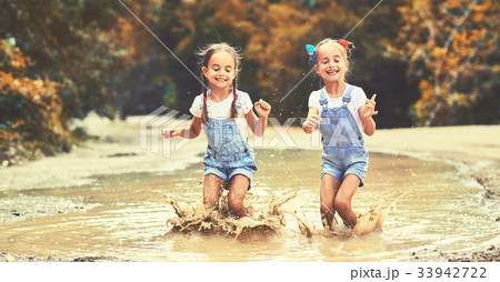 Happy funny sisters twins child girl   jumping on puddles in rubber boots  . 33942722