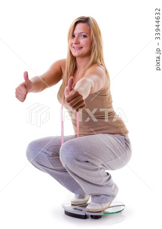 Happy woman wearing tracksuit squating on weighing machine Happy woman wearing tracksuit squating on weighing machine 33944632