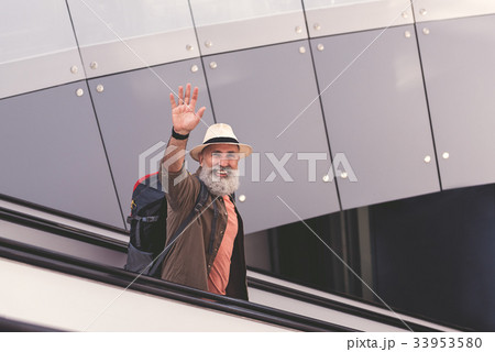 Cheerful pensioner waving with hand on escalator 33953580