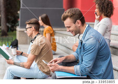 Happy male student entertaining with gadget near Happy male student entertaining with gadget near 33953805