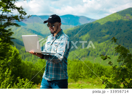 guy smiling and working on laptop in the mountains guy smiling and working on laptop in the mountains 33956714