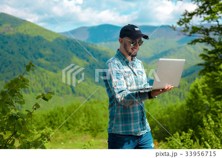 guy smiling and working on laptop in the mountains guy smiling and working on laptop in the mountains 33956715