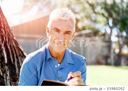 Senior man sittingin park while reading book Senior man sittingin park while reading book 33960262