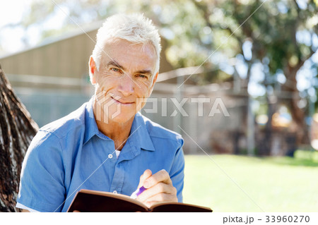 Senior man sittingin park while reading book Senior man sittingin park while reading book 33960270