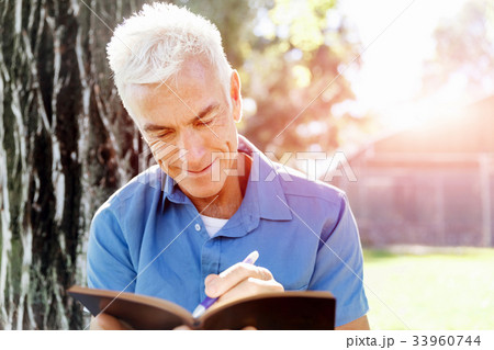 Senior man sittingin park while reading book 33960744