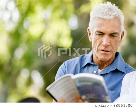 Senior man sittingin park while reading book 33961500