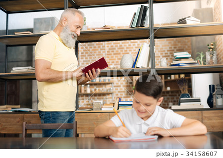 Smiling schoolboy doing homework while his Smiling schoolboy doing homework while his 34158607