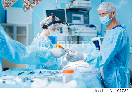 Serious mature doctor giving gone instrument Serious mature doctor giving gone instrument 34167785
