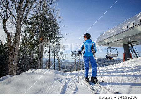 Female skier against ski-lift and winter mountains background 34199286