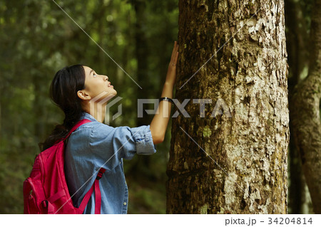 a young woman is touching the tree in the forest. 34204814