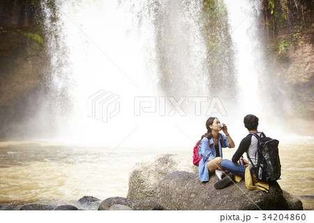 A couple is resting on the rock near the waterfall. A couple is resting on the rock near the waterfall. 34204860