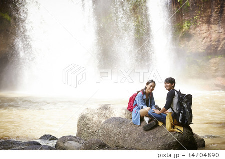 A happy couple is sitting on the rock near the waterfall. 34204890