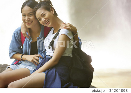 two female hikers are sitting side by side and arm in arm in the forest. two female hikers are sitting side by side and arm in arm in the forest. 34204898