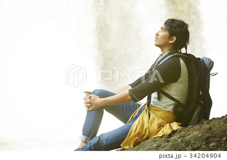 a man is sitting on the rock near the waterfall. 34204904