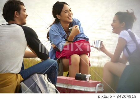 Three young people are talking and resting together on the riverside. 34204918