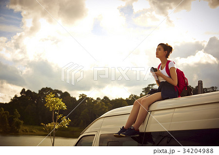 A girl is sitting on a rooftop of the van and enjoying views of the nature 34204988