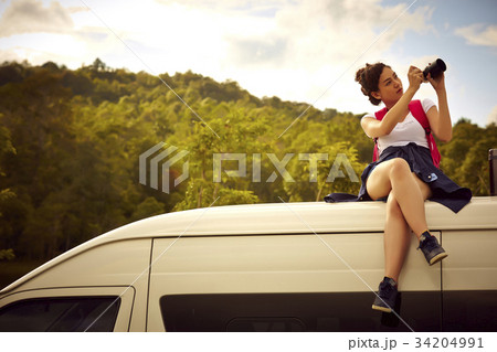 A girl is sitting on a top of a car, taking a photo of the nature by a digital camera 34204991