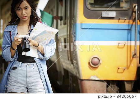 an asian girl is walking near the train and holding map and camera 34205067